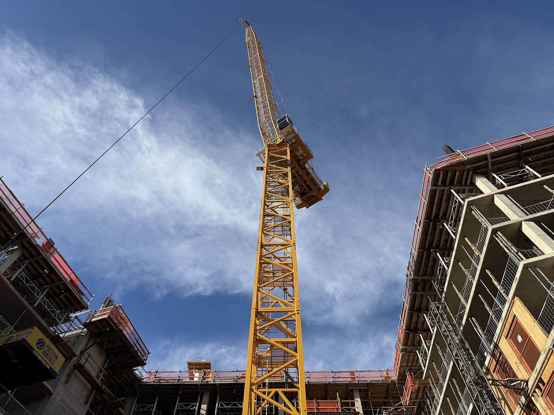 Tower crane rising above a multi-story building under construction against a clear blue sky